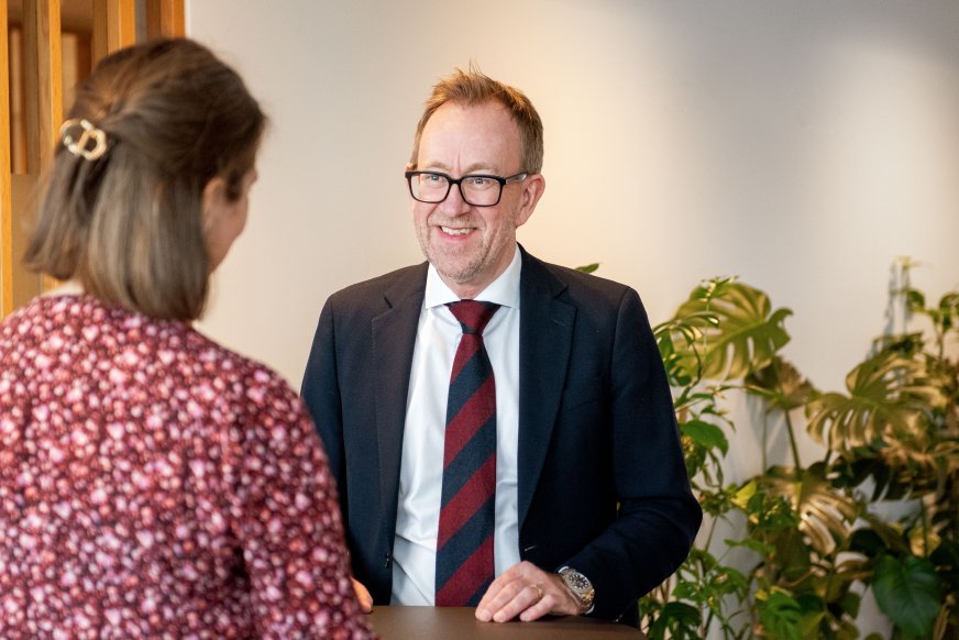 Billede af koncernchefen i GK, Kim Robert Lisø, i samtale med ansat i GK, taget indendørs med planter i baggrunden.