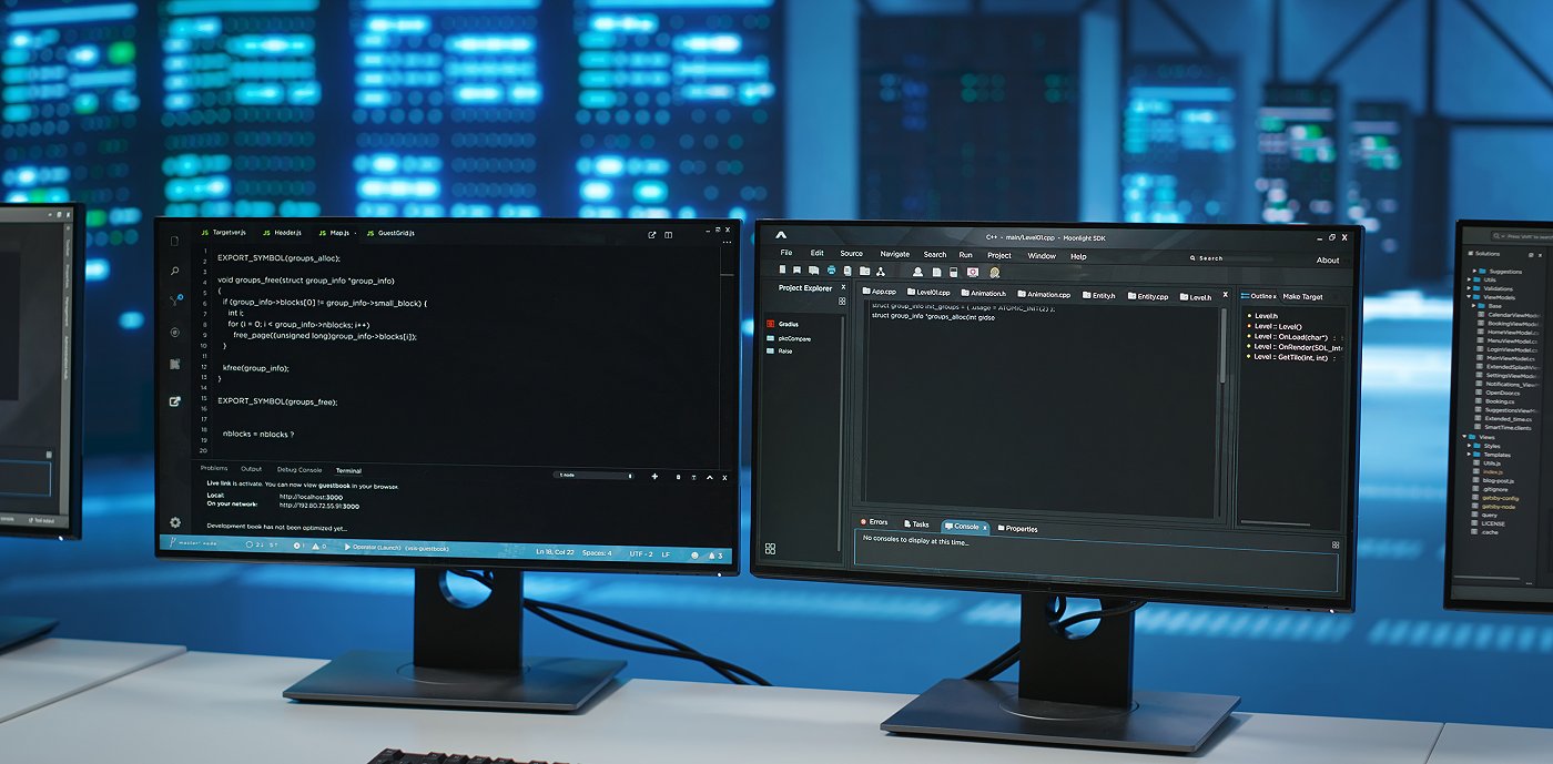 To tændte computerskærme placeret på et skrivebord med et tastatur og en mus. To tændte computerskærme placeret på et skrivebord med et tastatur og en mus.