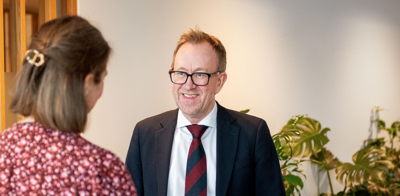 Billede af koncernchefen i GK, Kim Robert Lisø, i samtale med ansat i GK, taget indendørs med planter i baggrunden.